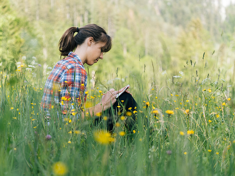Student writing in meadow with spring flowers