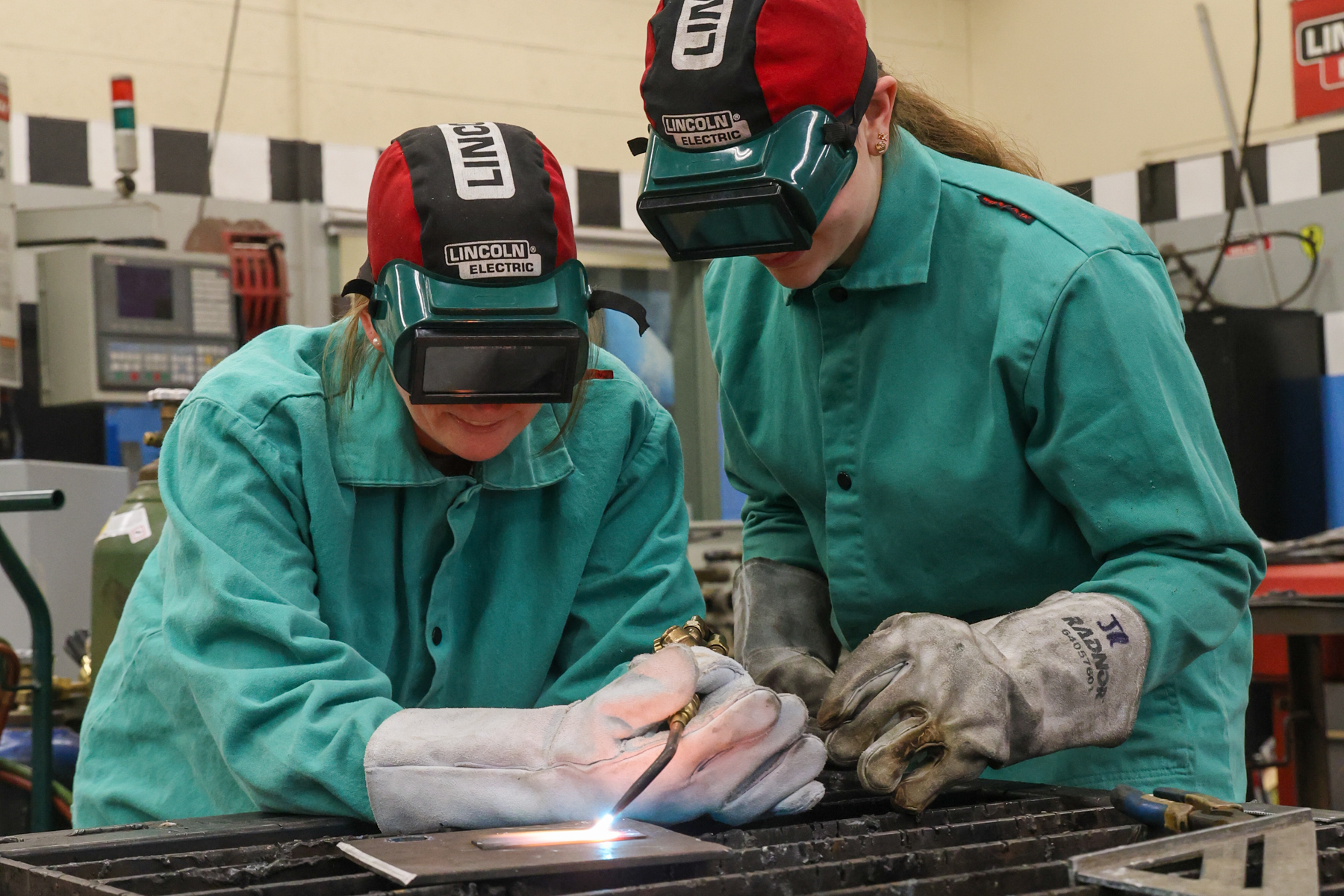 a woman welding with a student giving her instructions.