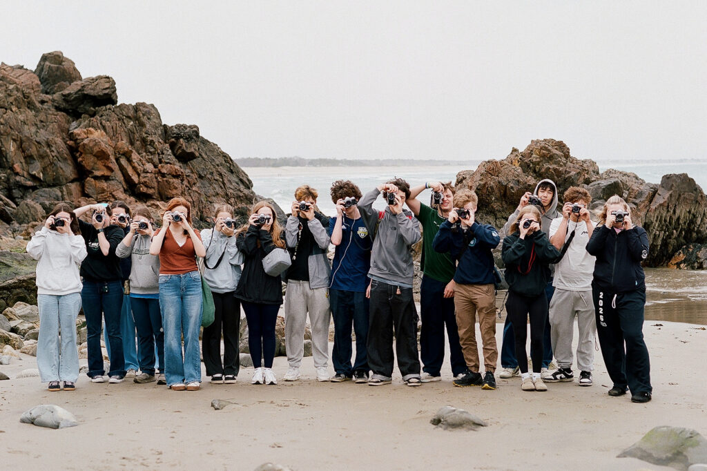Students taking photos on a beach by the ocean.