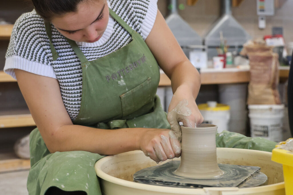 Student creating a mug on the wheel in ceramics.
